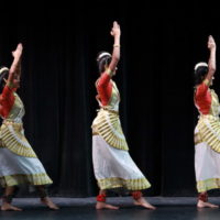 Three Mohiniyattam dancers in traditional white costumeswith arms raised